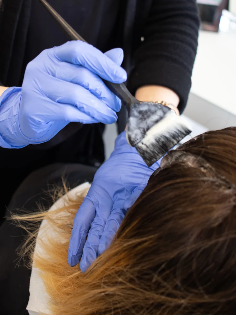Farbe wird mit dem Pinsel ins Haar einer Kundin eingearbeitet